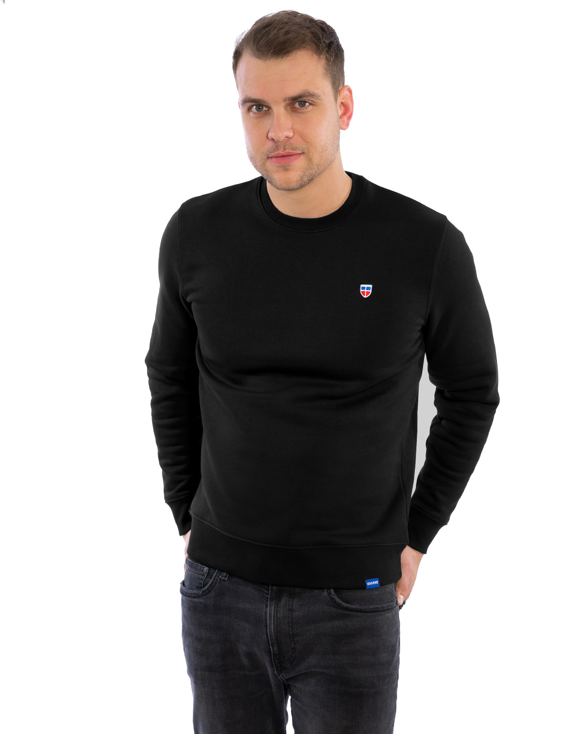 Auf dem Bild zusehen ist ein eleganter Sweater in schwarz. Der Sweater ist schlicht geschnitten und hat vorne links auf der Brust das LASARRE-Logo. Unten am linken Saum ist ein blaues Schildchen mit der weißen Aufschrift LASARRE.