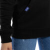 Detail-Ansicht der Kängurutasche des hochwertig bestickten sommerlich dünnen LASARRE Frauen Hoodie „MICHELLE“ in der Farbe Schwarz von der Saarland Marke Lasarre mit dem LASARRE Wappen in Blau, Weiß, Rot auf der linken Brust und dem blauen LASARRE Markenzeichen am Saum