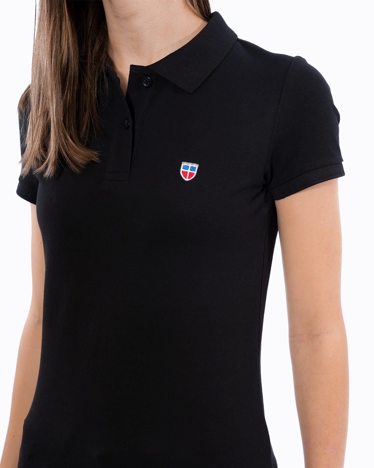 Vorderansicht des schwarzen Ladies-Polo-Shirt der Saarland-Marke LA SARRE. Nahaufnahme: Im Vordergrund stehen das gestickte Sarre-Wappen auf der linken Brust sowie das blaue Saumlabel mit der Aufschrift LA SARRE. Die Struktur des Piqué-Stoffs wird deutlich.