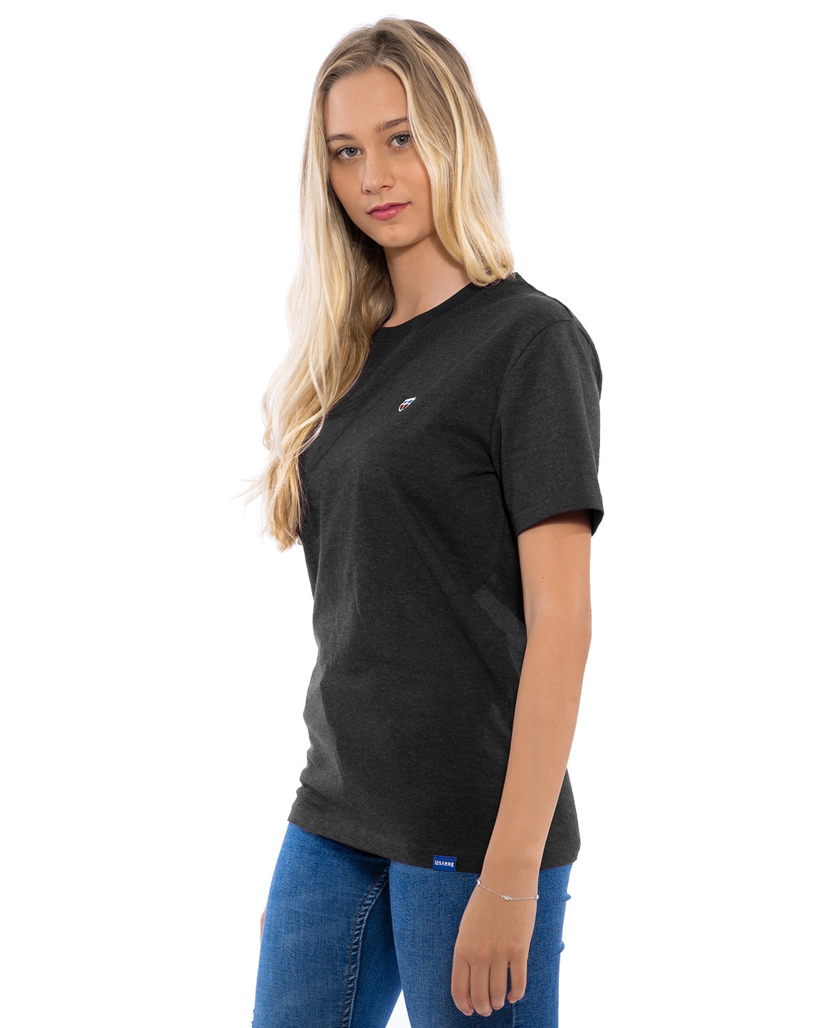 Junges weibliches Model in lässiger Pose im lava-grauen T-Shirt der Saarland-Marke LA SARRE. Perspektivische Ansicht. Auffällig sind das blaue LA SARRE Saumlabel und das Sarre-Wappen als Stickerei auf der Brust.