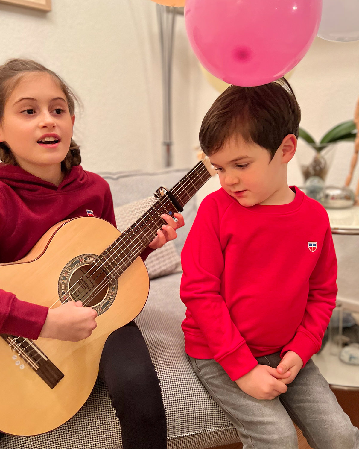 Wir sehen Anton, 5 Jahre alt in unserem Kinder Pullover Tom mit Saarland Wappen auf der linken Brust, der Seiner Schwester Leni beim Gitarre Spielen zusieht. Leni macht vor, wie es geht.