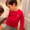 Wir sehen Anton, 5 Jahre alt in unserem Kinder Pullover Tom mit Saarland Wappen auf der linken Brust, der Seiner Schwester Leni beim Gitarre Spielen zusieht.