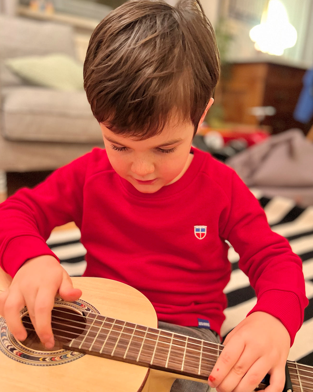 Wir sehen Anton, 5 Jahre alt in unserem Kinder Pullover Tom mit Saarland Wappen auf der linken Brust. Anton stimmt gerade eine Gitarre.