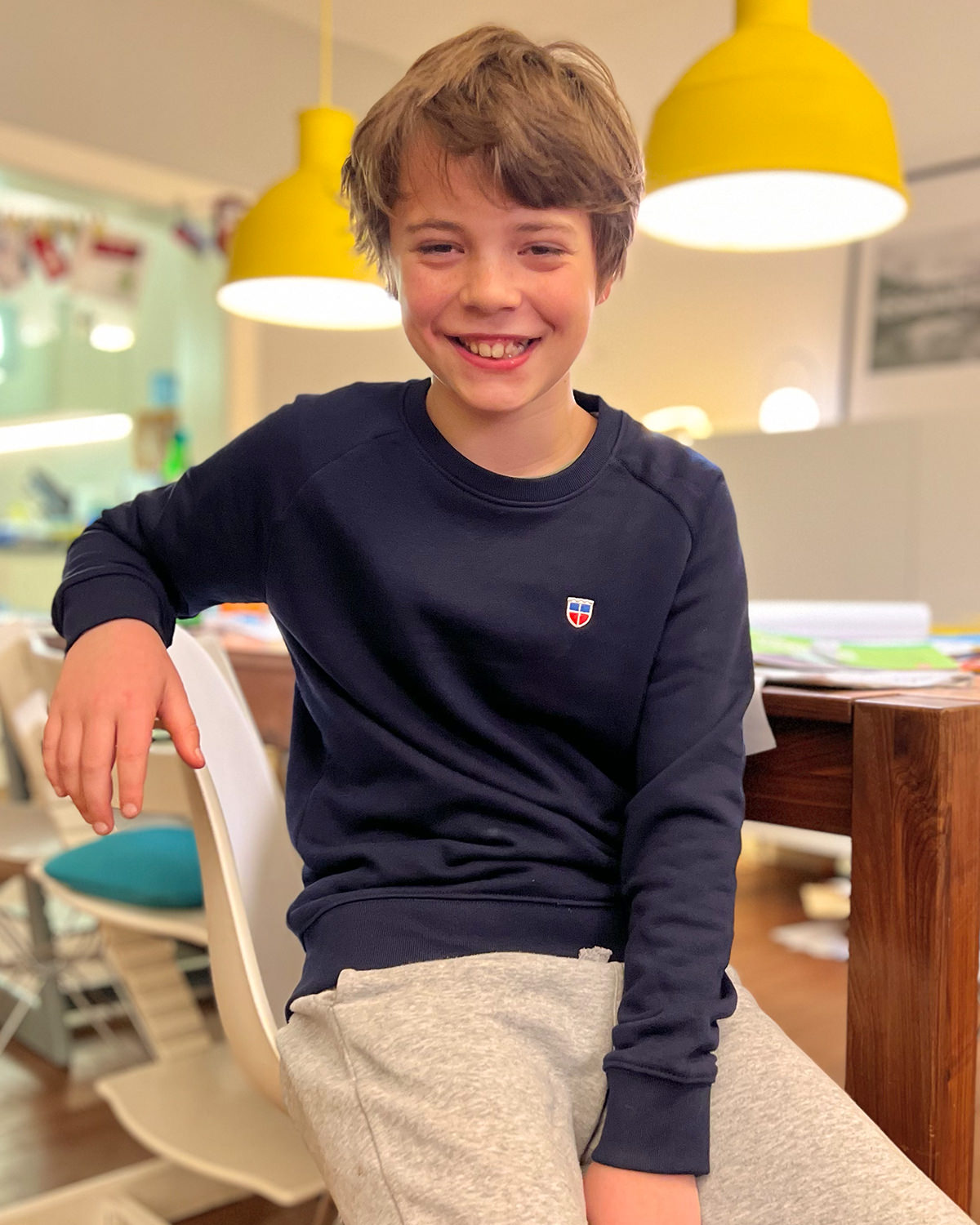 Saarland-Kinder-Sweatshirt Modell Tom von LA SARRE in Navy-Blau. Getragen von Paul. Der sitzt auf einem Stuhl, lächelt direkt in die Kamera und sieht richtig happy aus mit seinem neuen Sweatshirt.
