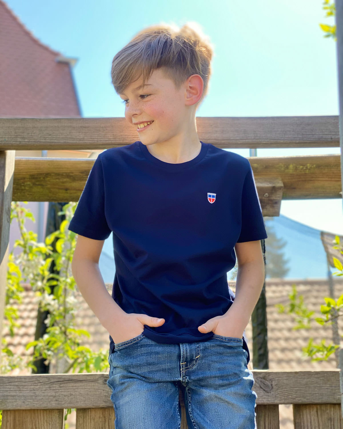Max, ein echtes Saarland Kind, lehnt lässig an der Brüstung seines Baumhauses. Er trägt unser Kinder T-Shirt Pascal in Navy-Blau.