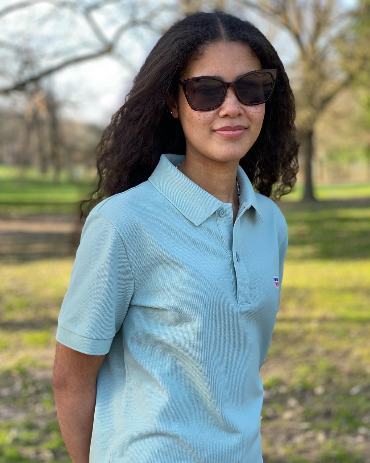 Saarland Geschenk T-Shirt. Jessi trägt das gerade geschnittene Unisex-Poloshirt GISÈLE mit Saarwappen in der Farbe Pistache.