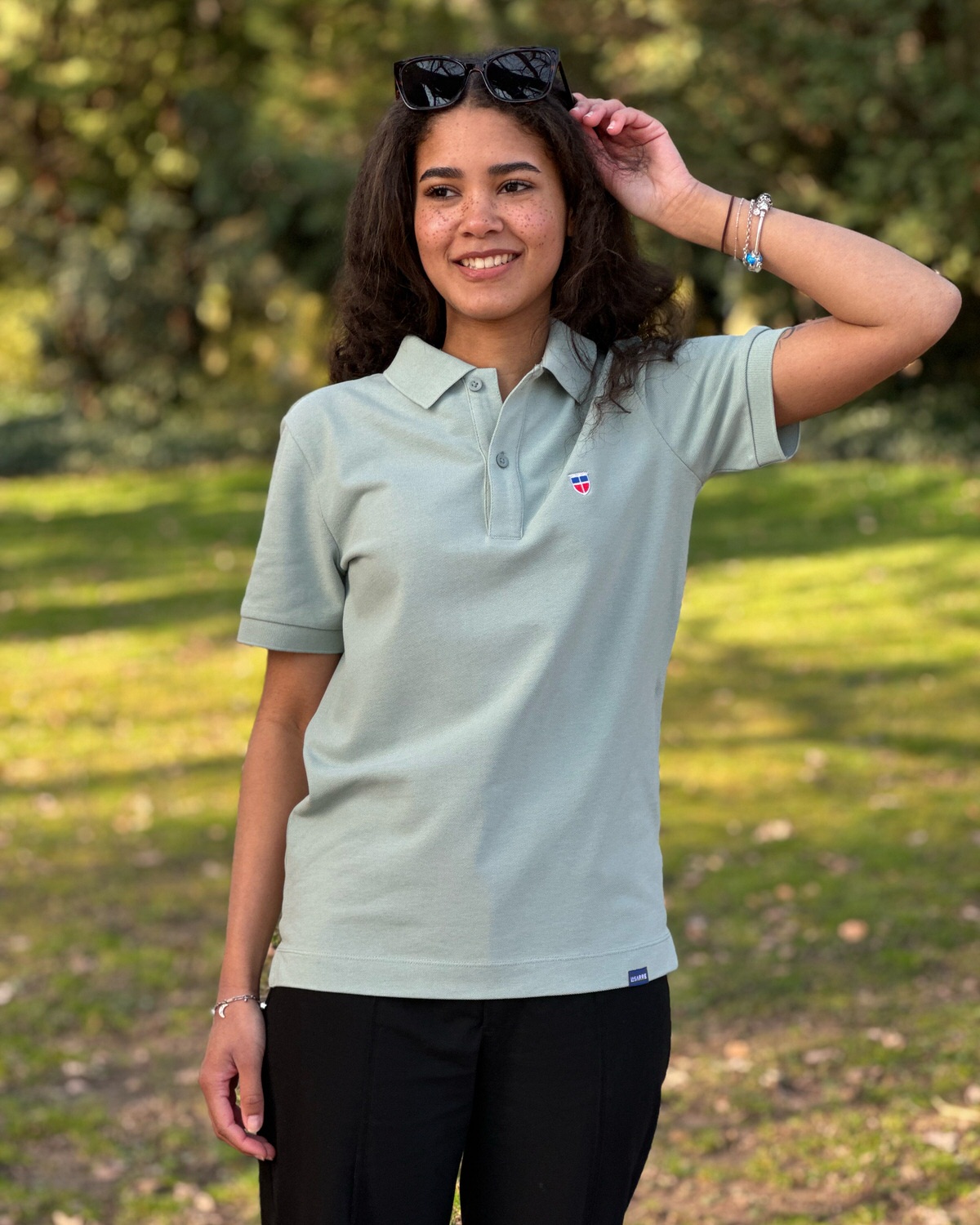 Saarland Geschenk T-Shirt. Jessi trägt das gerade geschnittene Unisex-Poloshirt GISÈLE mit Saarwappen in der Farbe Pistache.
